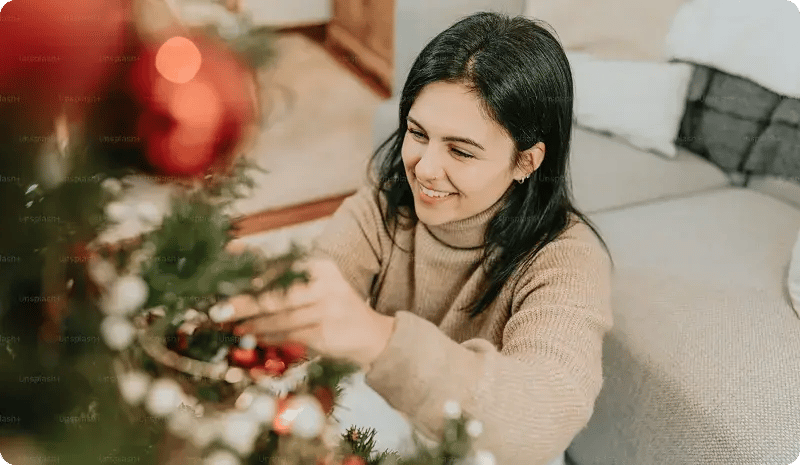 Mujer joven decorando un árbol de Navidad en casa.
