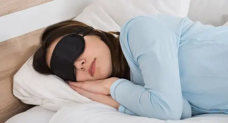 Mujer descansando en la cama con antifaz para dormir.