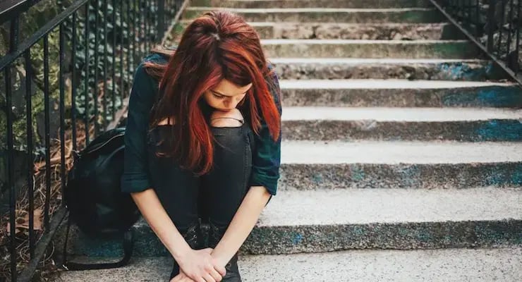 Mujer sentada en unas escaleras con la cabeza inclinada y los brazos apoyados sobre las piernas.