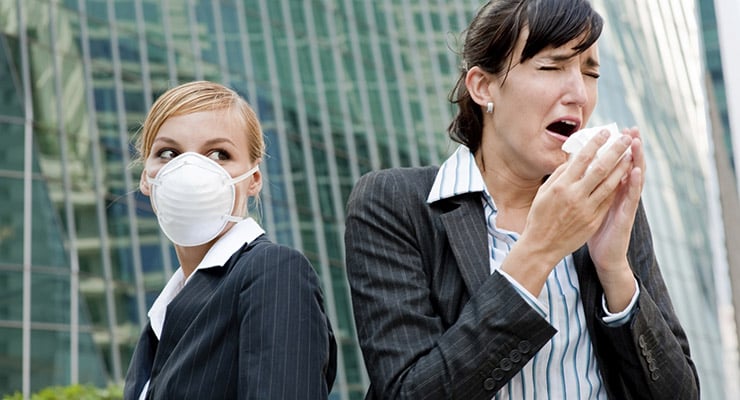 Dos mujeres en un entorno urbano, una usando mascarilla y otra estornudando con un pañuelo
