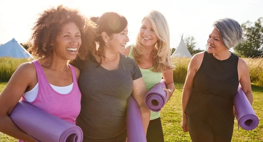 Grupo de mujeres adultas sonrientes con tapetes de yoga iniciando actividad física al aire libre