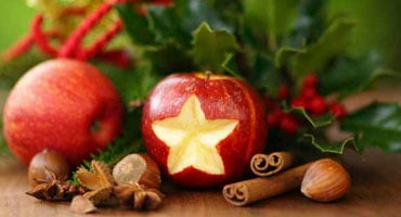 Manzanas rojas, canela y nueces decoradas con motivos navideños, representando opciones de alimentación saludable para diabéticos en Navidad.