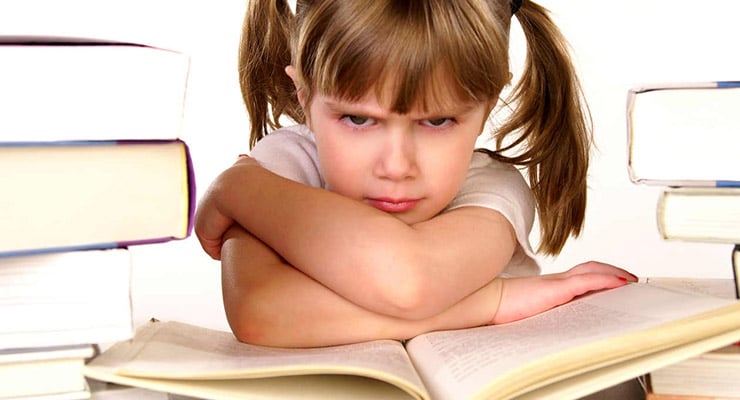 Niña sentada frente a un libro abierto con los brazos cruzados y libros a los lados