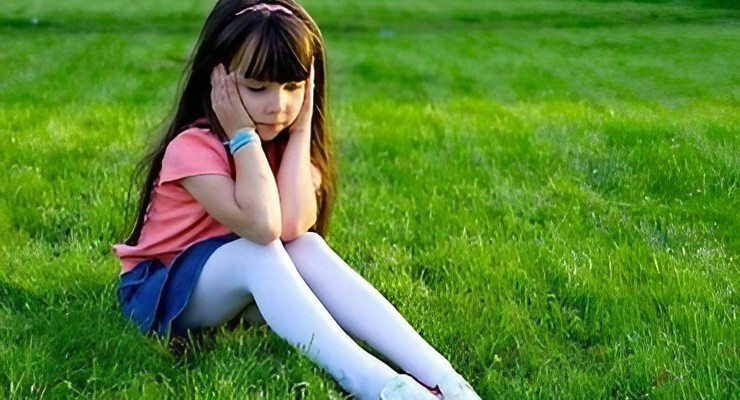 Niña sentada sobre el césped con la cabeza apoyada en las manos en un espacio al aire libre