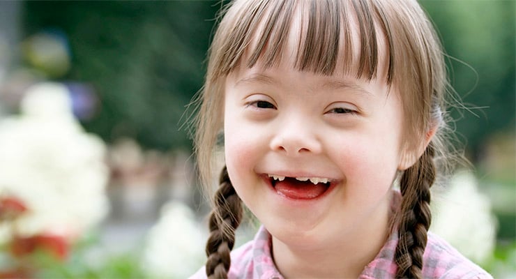 Niña sonriendo al aire libre con trenzas y blusa a cuadros en un entorno natural.