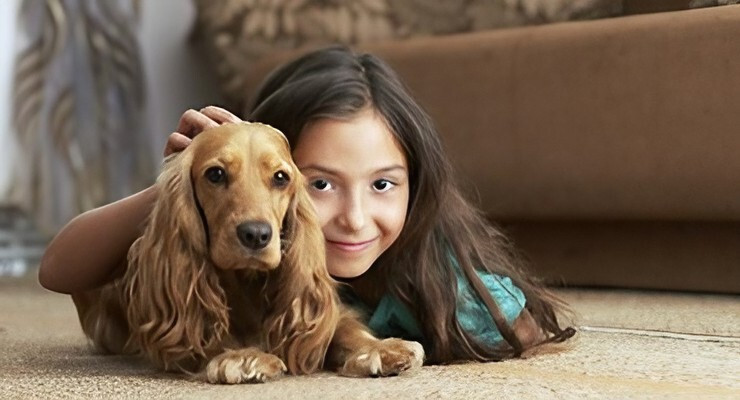 Niña acostada junto a su perro dentro de una casa