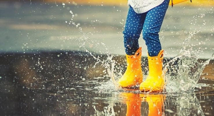 Niño usando botas impermeables mientras salta en un charco durante la lluvia