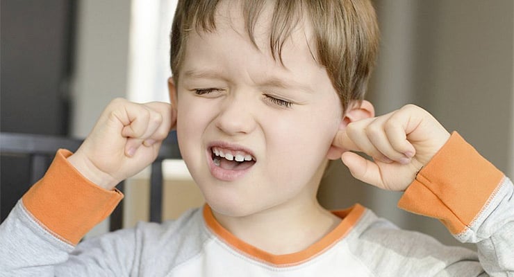 Niño con los ojos cerrados tapándose los oídos por dolor