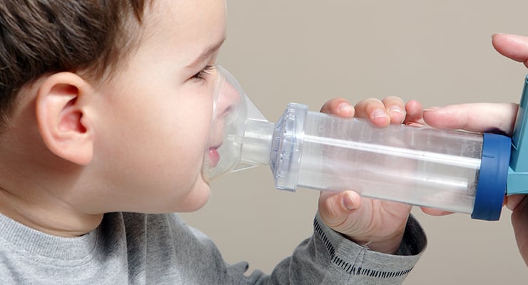 Niño pequeño utilizando un inhalador con cámara espaciadora y mascarilla