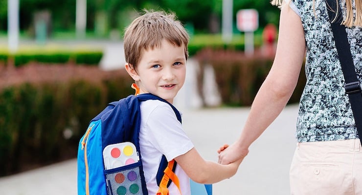 Niño con mochila escolar toma la mano de un adulto camino a la escuela