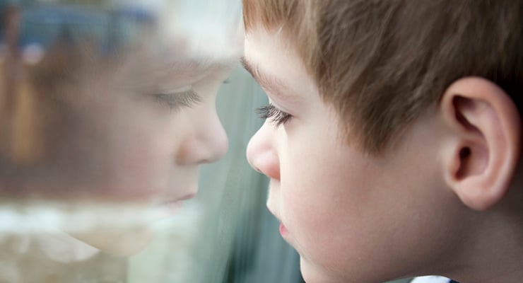 Niño de perfil observando su reflejo en una ventana de vidrio.