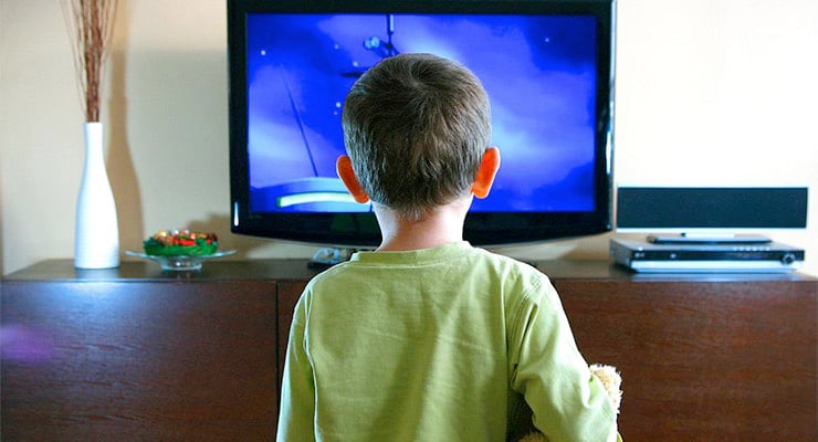 Niño de espaldas observando la televisión encendida en la sala de una casa