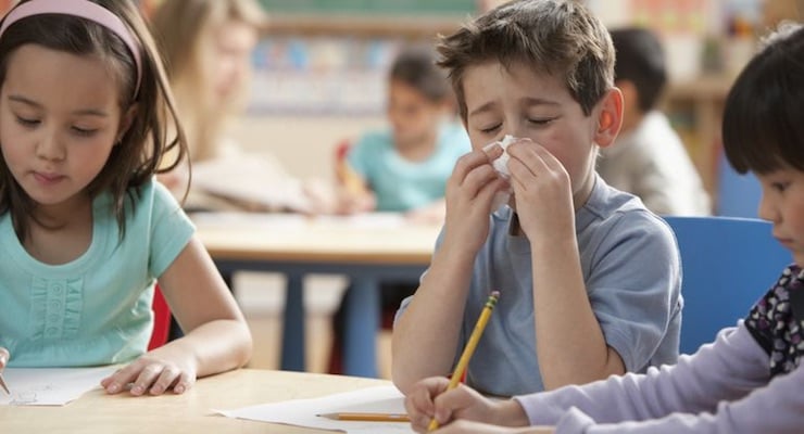 Niños en un aula escolar mientras uno se limpia la nariz durante la clase
