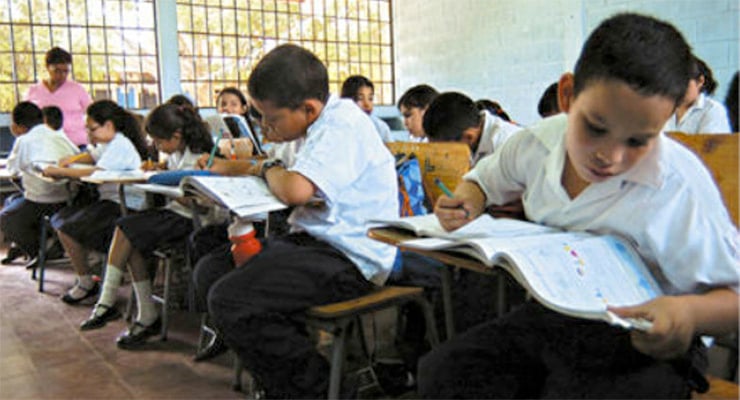 Niños sentados en un aula escolar escribiendo en sus cuadernos durante la clase