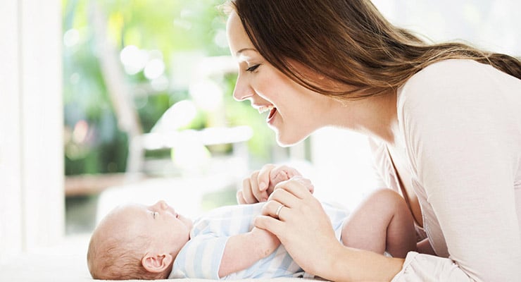Madre acostada sonriendo mientras sostiene y mira a su bebé recién nacido