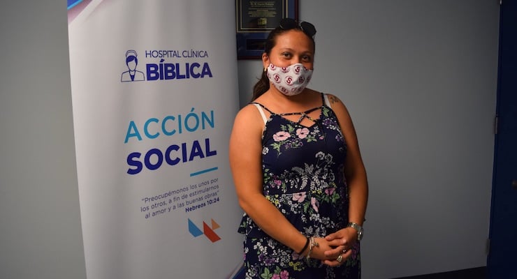 Mujer beneficiaria de la campaña de salud posa junto al banner informativo del Programa de Acción Social.