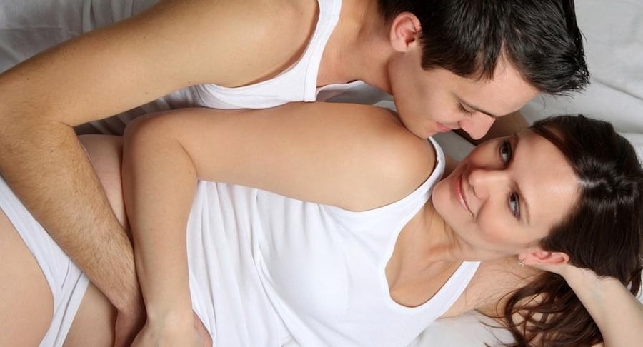 Pareja joven en la cama abrazada tiernamente, representando la intimidad y la vida sexual saludable durante la etapa del embarazo.