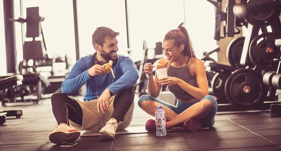 Pareja joven en el gimnasio comiendo y bebiendo después del entrenamiento