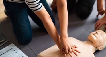 Estudiantes en una sesión de capacitación de primeros auxilios practicando compresiones torácicas de RCP sobre un maniquí de entrenamiento médico.