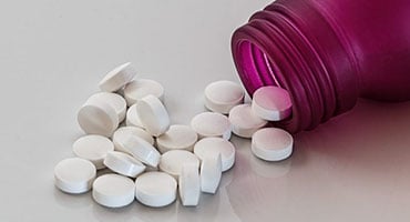 Frasco de color púrpura volcado con pastillas blancas circulares, representando suplementos bloqueadores de carbohidratos.