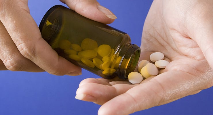 Mano sosteniendo pastillas mientras se vierten desde un frasco de medicamento