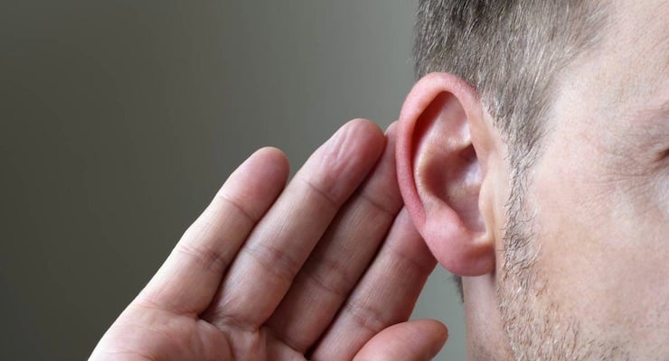 Primer plano del oído de un hombre con la mano detrás de la oreja en gesto de dificultad para escuchar.