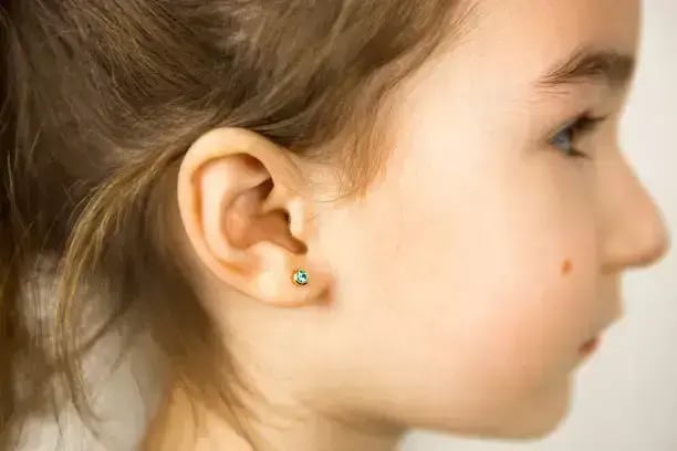 Perfil de niña con arete verde en la oreja después de perforación segura