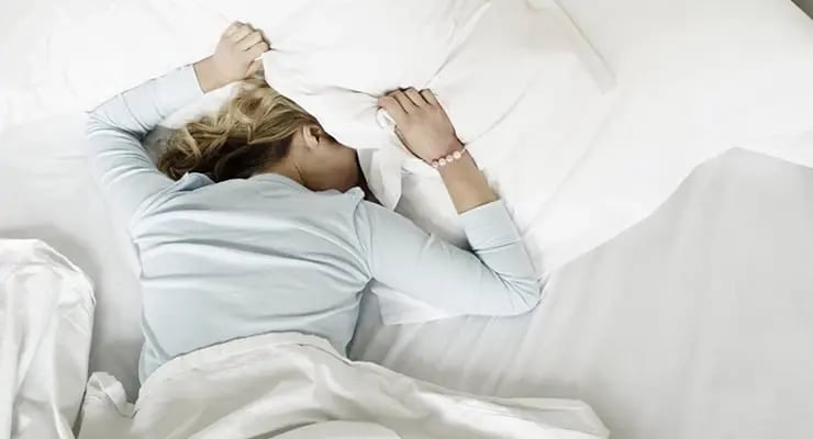 Persona acostada en una cama moviéndose entre las sábanas