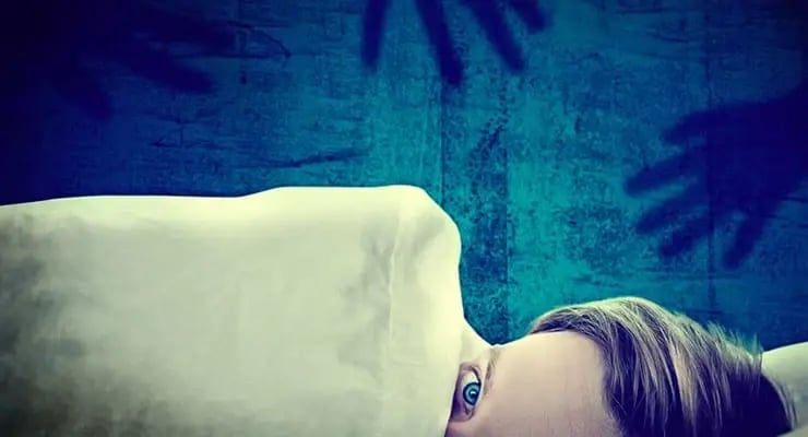 Persona acostada en una cama con los ojos abiertos parcialmente cubierta por una sábana