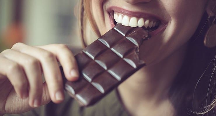 Persona mordiendo una barra de chocolate sostenida con la mano.