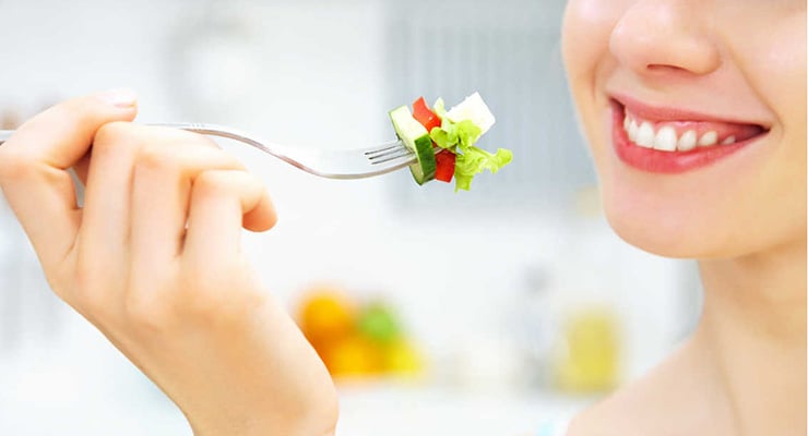 Persona sonriendo mientras lleva un bocado de ensalada con un tenedor a la boca.