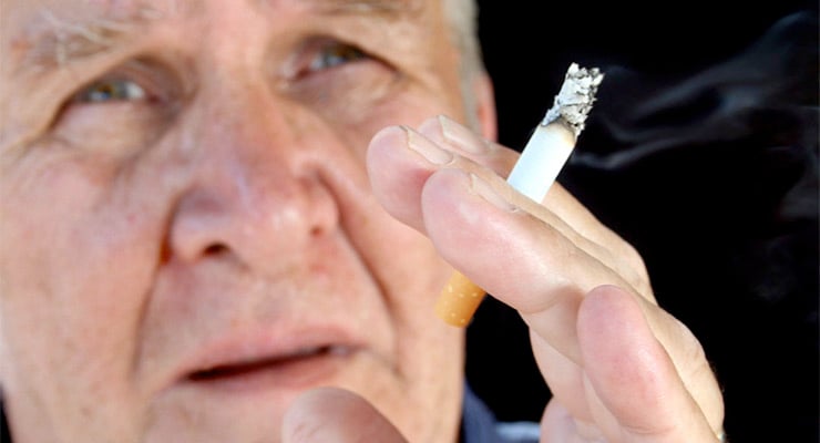Persona adulta sosteniendo un cigarrillo encendido cerca del rostro.