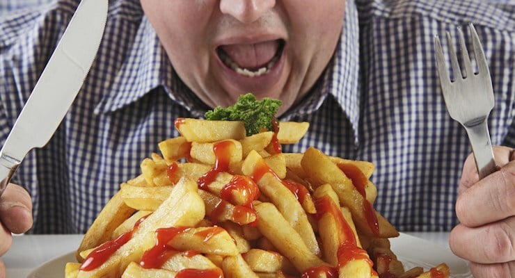 Persona frente a un plato con papas fritas y salsa, sosteniendo un cuchillo y un tenedor