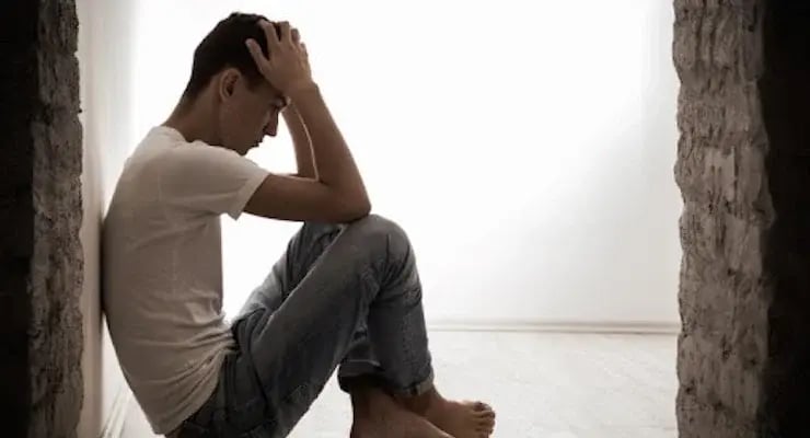 Persona joven sentada en el suelo con gesto de preocupación en un espacio interior iluminado.
