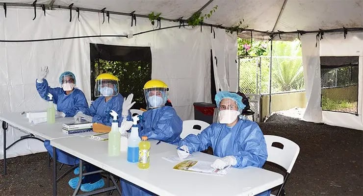 Personal de salud con equipo de protección atendiendo en una mesa dentro de una carpa.