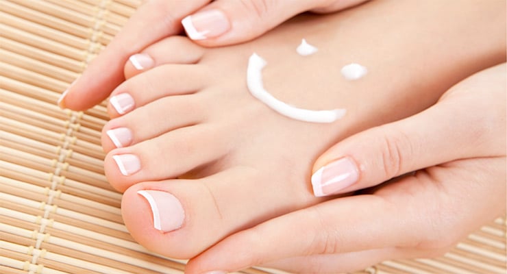 Pies con uñas cuidadas mientras se aplica crema hidratante sobre el empeine.