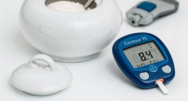 Un glucómetro digital mostrando un nivel de azúcar en sangre elevado junto a un azucarero, simbolizando los riesgos de la prediabetes y el consumo de azúcar.