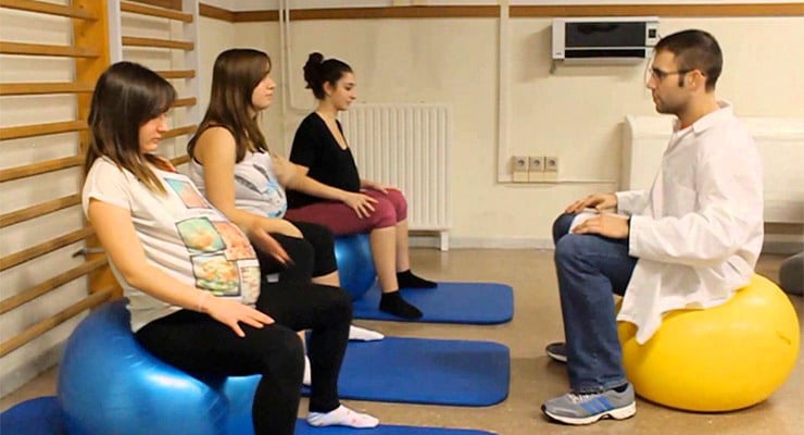 Mujeres embarazadas realizando ejercicios de preparación para el parto con un instructor en sala de maternidad.