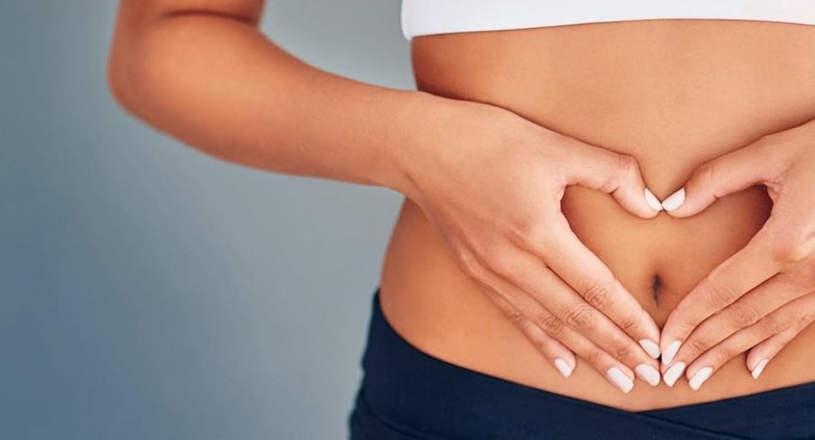 Primer plano de una mujer formando un corazón con sus manos sobre su vientre, representando salud ginecológica y bienestar postoperatorio.