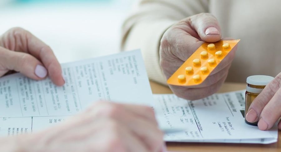Primer plano de un profesional de la salud entregando un blíster de pastillas a un paciente mientras revisan juntos una receta médica.
