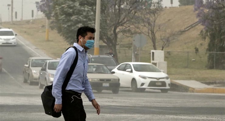 Persona caminando en la vía pública usando mascarilla debido a la presencia de ceniza volcánica en el ambiente.