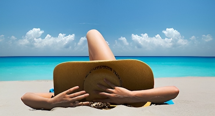Persona recostada en la playa usando sombrero para protegerse del sol