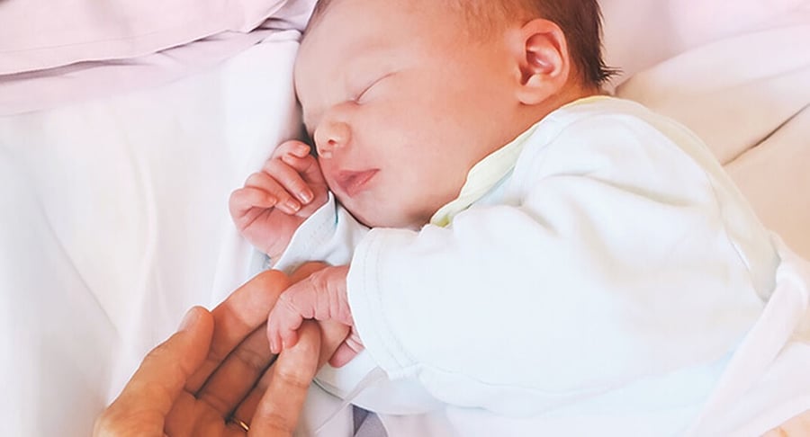 Recién nacido dormido sosteniendo el dedo de un adulto sobre una cama blanca