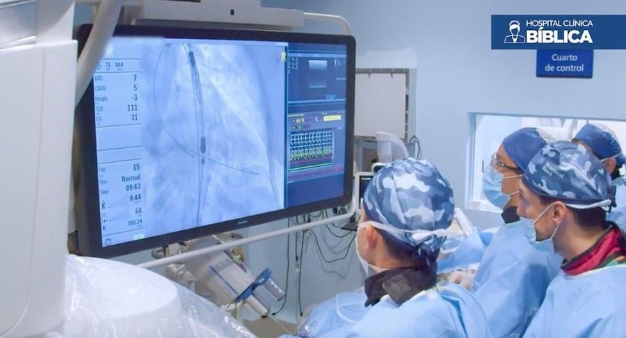 Equipo de cardiólogos del Hospital Clínica Bíblica en un cuarto de control observando imágenes de rayos X en tiempo real durante un procedimiento de reemplazo de válvula aórtica.