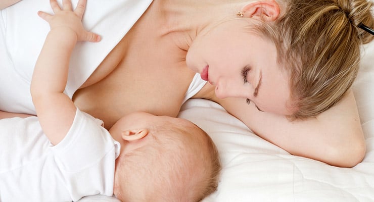Madre acostada amamantando a su bebé mientras ambos descansan
