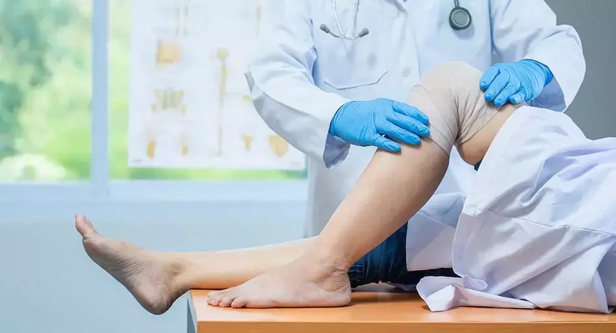 Médico revisando la rodilla vendada de un paciente en proceso de rehabilitación