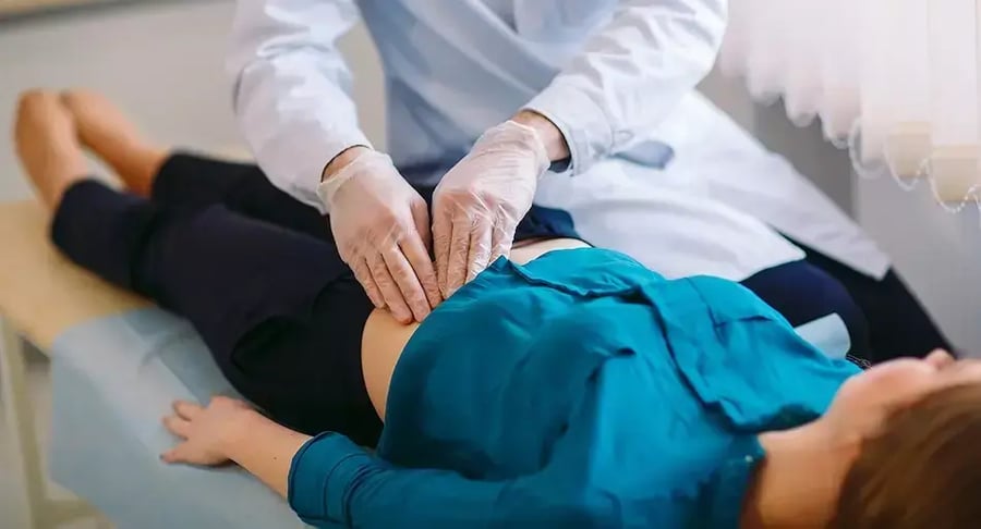 Médico examinando el abdomen de una paciente recostada en camilla