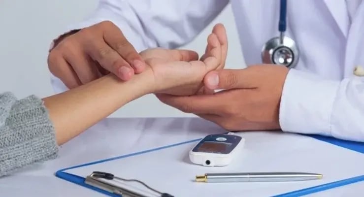 Médico revisando pulso de paciente con glucómetro sobre la mesa en control de prediabetes