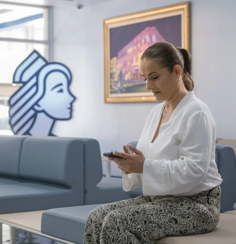 Woman sitting in the waiting room of Clínica Bíblica using her cell phone.