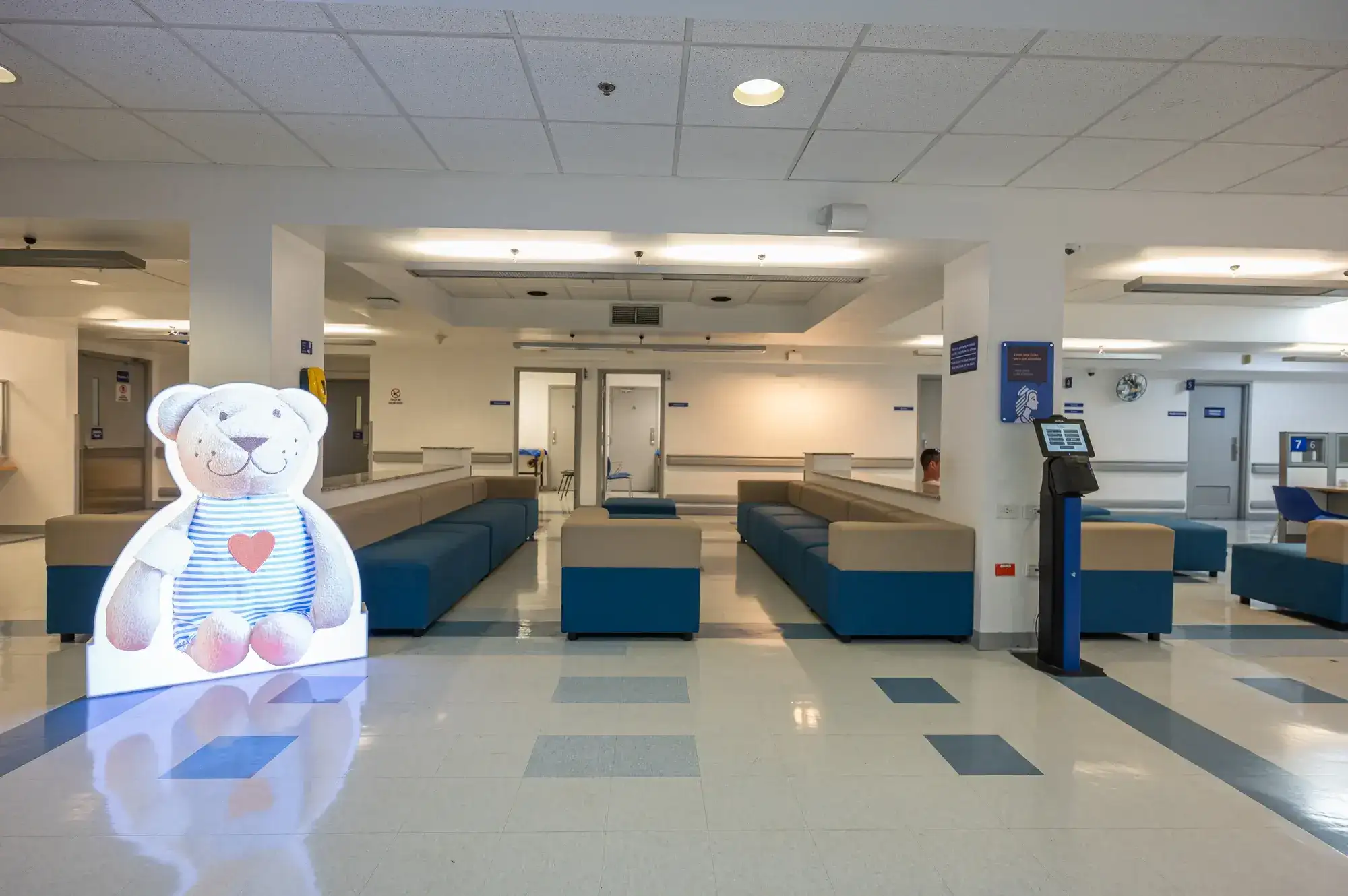 Hospital waiting room with blue and beige armchairs, children's decoration with teddy bear.